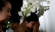 Thai mourners hold flowers as they offer prayers outside the Grand Palace, where the late King Bhumibol Adulyadej is lying in state in Bangkok on October 16, 2016. / AFP / MANAN VATSYAYANA