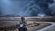 An Iraqi soldier and a civilian ride a motorbike as smoke rises behind them, on the road between Qayyarah and Mosul on October 28, 2016.  AFP / BULENT KILIC
