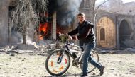 A Syrian youth pushes his bicycle past a burning house on November 19, 2016 following a reported air strike on Aleppo's rebel-held neighbourhood of Bab al-Nayrab. AFP / AMEER ALHALBI