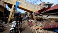 This picture taken on December 12, 2016 shows two girls on a motorcycle as they pass a collapsed building after a 6.5-magnitude earthquake struck the town of Pidie, Indonesia's Aceh province in northern Sumatra, on December 7, 2016.  AFP / CHAIDEER MAHYUD