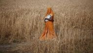 A woman carries her baby as she walks through a wheat field, in Amroha district in Uttar Pradesh April 17, 2014. REUTERS/Adnan Abidi/File Photo