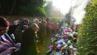 People gather and pause outside the home of British singer George Michael where tributes of flowers, messages and candles have been piled in the village of Goring, southern England, yesterday.