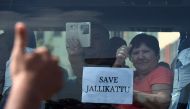 A foreign tourist raises her thumb and holds a placard against the car window as she passes students during a demonstration against the ban on the Jallikattu bull taming ritual and a call for a ban on animal rights orgnisation PETA, in Chennai on January 