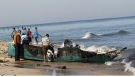 Palestinian fishermen inspect their destroyed fishing boat hauled up onto the shore, close to the southern Gaza Strip town of Rafah, on March 26, 2014. Several Palestinians were wounded when Israeli navy vessels shot at two Gaza-bound boats smuggling ciga