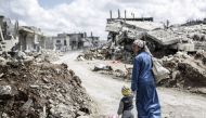 A Kurdish Syrian woman walks with her child past the ruins of the town of Kobane, also known as Ain al-Arab, on March 25, 2015. / AFP.