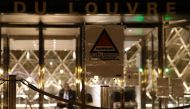 A security guard sits at the entrance of the Louvre Pyramid of the Louvre museum in Paris, on February 3, 2017, as a sign with the symbol of France's national security alert system 