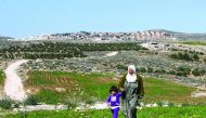 A Palestinian woman and a child walking in the Bani Naaim village with the Israeli settlement of Bani Hever, southwest of the Israeli occupied West Bank city of Hebron, seen in the background.