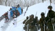 Firefighters carry a survivor they rescued from the site of an avalanche in Nasu town, Tochigi prefecture on March 27, 2017, while Self Defense Force personnel look on.  AFP / JIJI PRESS
