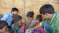 This picture taken on April 7, 2017 shows Anand Solanki (R), facilitator of the 'Zero Connect' programme, and teacher Deepsinh Vanola (top L), with a group of children of salt pan workers during a tent school workshop using an Internet-connected van, in t