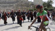 A cyclist rides past a group of traditional dancers at the ancient Roman theatre in the centre of Amman during a welcome ceremony for members of the Middle East Peace Tour pre-Event on April 24, 2017. AFP / Menahem Kahana
