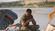 A member of the US-backed Syrian Democratic Forces (SDF), made up of an alliance of Arab and Kurdish fighters, sits on the edge of a boat at the Tabqa dam on April 29, 2017. AFP / DELIL SOULEIMAN
