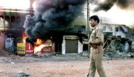 This file photograph taken March 1, 2002, shows an Indian policeman as he walks in front of a row of burning shops in Ahmedabad.