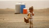 A displaced child, who fled from the Islamic State (IS) group bastion of Raqa, stands outside as she eats a loaf of bread in a camp for displaced near the town of al-Karamah, 26 kms from Raqa, on May 10, 2017. / AFP / DELIL SOULEIMAN