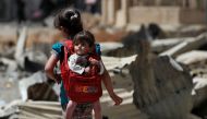 An Iraqi girl carries a baby in a backpack turned into a baby carrier as displaced Iraqis from western Mosul's al-Islah al-Zaraye neighbourhood flee their area on May 12, 2017 during a government forces' military offensive to retake the area from Islamic 