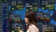 A woman walks past a quotation board displaying numbers of the world stock markets in front of a securities company in Tokyo on May 15, 2017. / AFP.