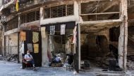 An elderly Syrian sits outside a newly-reopened shop amid the destruction, where he sells tablecloths in the old city of Aleppo on July 22, 2017. (AFP / George OURFALIAN)