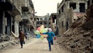 FILE PHOTO: Syrian children run with balloons past heavily damaged buildings in the neighbourhood of Jobar on the eastern outskirts of the Syrian capital Damascus on April 9, 2016 (AFP / Amer Almohibany) 
