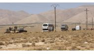 Syrian forces members stand on a tank next to vehicles waiting to transport Islamic State (IS) group members in the Qara area in Syria's Qalamoun region on August 28, 2017 as part of a deal between Hezbollah and IS fighters where the jihadists would leave
