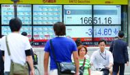 Pedestrians walking past an electric quotation board displaying the Nikkei key index of the Tokyo Stock Exchange in the file picture.
