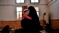 The wife of a suspected member of the Islamic State (IS) group holds her child as she waits on the western frontline to be questioned after fleeing the centre of Raqa, on October 8, 2017.  AFP / BULENT KILIC
