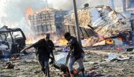 Two men carry the body of a victim following the explosion of a truck bomb in the centre of Mogadishu, on October 14, 2017. / AFP.