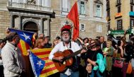 A man sporting a Catalan typical 'barretina' hat plays guitar as other people wave Catalan flags in front of the 'Generalitat' palace (Catalan government headquarters) in Barcelona on October 30, 2017.  AFP / LLUIS GENE

