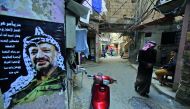 A Palestinian refugee walks at the Shatilla Palestinian refugee camp, on the southern outskirts of the Lebanese capital Beirut, yesterday. A poster showing late Palestinian leader Yasser Arafat is seen on the left. 