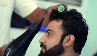 This photograph taken on October 12, 2017 shows a male hairdresser blow-drying a customer's hair at a men's salon in Islamabad. 