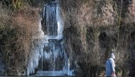 A pedestrian walks past a frozen waterfall hanging above a lake in The Orangerie Park in Strasbourg, eastern France on February 27, 2018. AFP / FREDERICK FLORIN