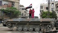 Syrian children hold a national flag while standing atop an infantry fighting vehicle (IFV) in the Eastern Ghouta town of Hazzeh on the outskirts of the Syrian capital Damascus, on March 28, 2018. / AFP / STRINGER
