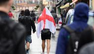 (FILES) In this file photo taken on June 16, 2016, a football supporter covers his head with an England flag, the St George's Cross, as he walks in the rain in Lens, northern France, on the day England played against Wales in their Euro 2016 group B footb