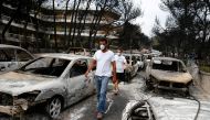 :Locals wearing masks walk among burnt cars following a wildfire at the village of Mati, near Athens, Greece, July 24, 2018. REUTERS/Costas Baltas
