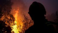 Firefighters watch trees burning in flames as they combat a wildfire close to Monchique in the Portuguese Algarve, on August 8, 2018.  / AFP / CARLOS COSTA 
