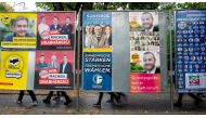 People pass behind election posters in Bolzano, Italy on October 15, 2018. AFP / Joe Klamar 