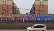 A car moves past a residential area separated by a wall carrying an advertisement of a local auto dealer, in Lushan county, Pingdingshan, Henan province, China November 16, 2018. Reuters/Yilei Sun