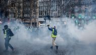 A protester wearing a yellow vest (gilet jaune) holds a bunch of flowers as he runs through smoke of tear gas during a demonstration against rising costs of living they blame on high taxes on the Champs-Elysees avenue in Paris, on December 15, 2018. AFP /