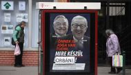 People walk past a poster on a telephone booth showing the portraits of European Commission chief Jean-Claude Juncker (R) and Hungarian-born US investor and philanthropist George Soros and a slogan reading 