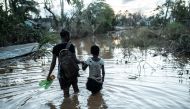 Rosita Moises Zacarias (L), 15, holding the hand of her sister Joaninha Manuel, 9, walks in flooded waters from their house destroyed by the cyclone Idai, to go to seep in a shelter in Buzi, Mozambique, on March 22, 2019.  AFP / Yasuyoshi CHIBA
