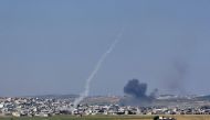 Smoke from an incoming shell (R) billows above buildings in the town of Kafr Nabuda as a rocket fired from the twon leaves a white trace of smoke, in the north of the Syrian Hama province during reported air strikes by Syrian regime forces on May 26, 2018