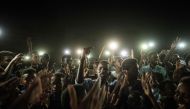 People chant slogans as a young man recites a poem, illuminated by mobile phones, before the opposition's direct dialog with people in Khartoum on June 19, 2019.   AFP / Yasuyoshi CHIBA