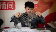 Jin Xinchun, a member of the Flying Dragon Troupe, creates a shadow puppet at the troupe's studio on the outskirts of Beijing. AFP / NICOLAS ASFOURI