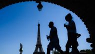 A man holding a bottle of water walks by a woman sipping a drink through a straw on a bridge over the Seine river in front of the Eiffel Tower in Paris on July 23, 2019. Parisians were bracing for potentially the hottest ever temperature in the French cap