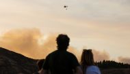 People who were evacuated from their homes look at a helicopter dropping water to fight a forest fire seen in the village of Valleseco, in the Canary Island of Gran Canaria, Spain, August 17, 2019. REUTERS/Borja Suarez