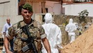 A Lebanese army soldier walks past military intelligence forensic investigators of inspecting the scene where two drones came down in the vicinity of a media centre of the Shiite Hezbollah movement earlier in the day, in the south of the capital Beirut on