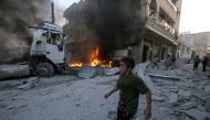 A young boy runs past a fire started in a building following a reported airstrike by Syrian regime forces in the town of Maaret al-Numan in Syria's northwestern Idlib province on August 28, 2019. / AFP / Abdulazez Ketaz
