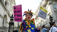 An anti-Brexit protester wearing a clown costume and a defaced mask depicting Boris Johnson holds placards in Westminster in London, Britain August 29, 2019. Reuters/Toby Melville