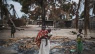 A woman holds her younger child while standing in a burned out area in the recently attacked village of Aldeia da Paz outside Macomia, on August 24, 2019.  AFP / Marco Longari 