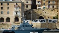 A Malta Coast Guards ship patrols as protesters display a banner reading 