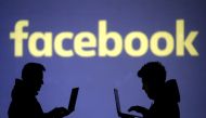 Silhouettes of laptop users are seen next to a screen projection of Facebook logo in this picture illustration dated  March 28, 2018. Reuters/Dado Ruvic