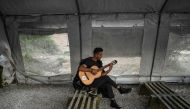 File photo: A man plays the guitar at an unofficial camp outside the refugee camp of Moria on the Greek island of Lesbos on March 19. 2019. AFP / Aris Messinis